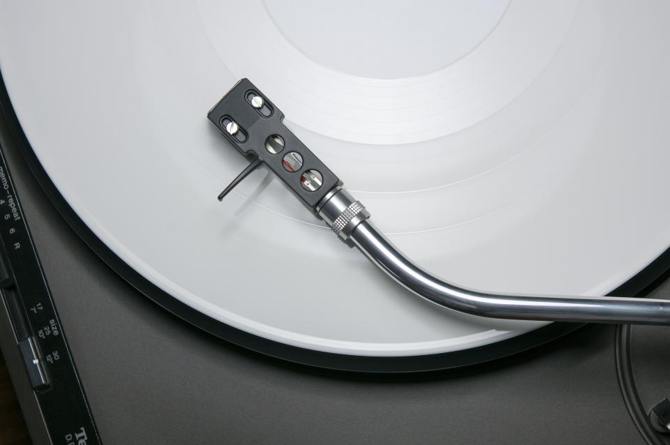 A tonearm and cartridge over a white vinyl record on a turntable.